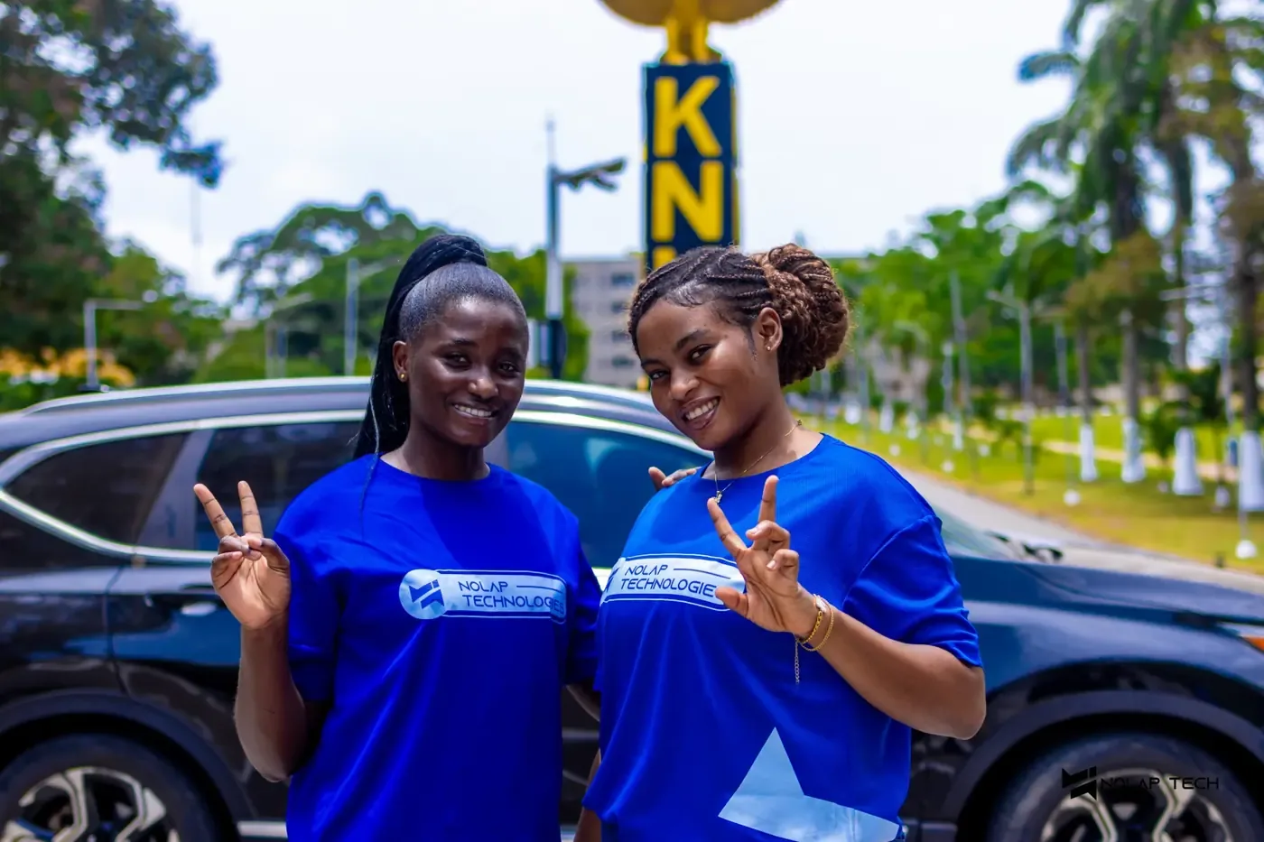Two NOLAP team members in blue shirts smiling and making peace signs