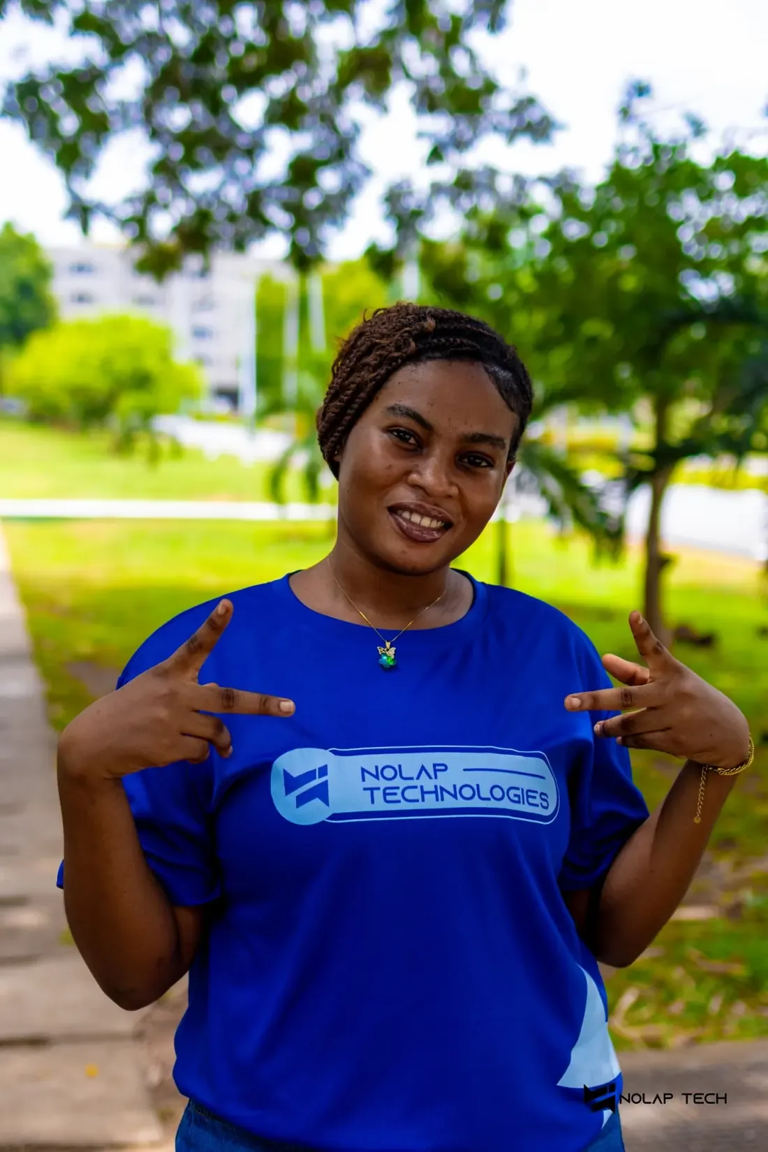 A NOLAP team member smiling and pointing to the NOLAP Technologies logo on her blue shirt